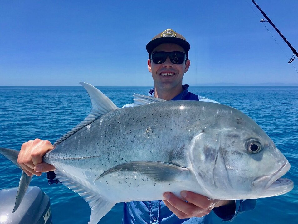Game fisherman showing a trevally fish with blue skies and calm waters