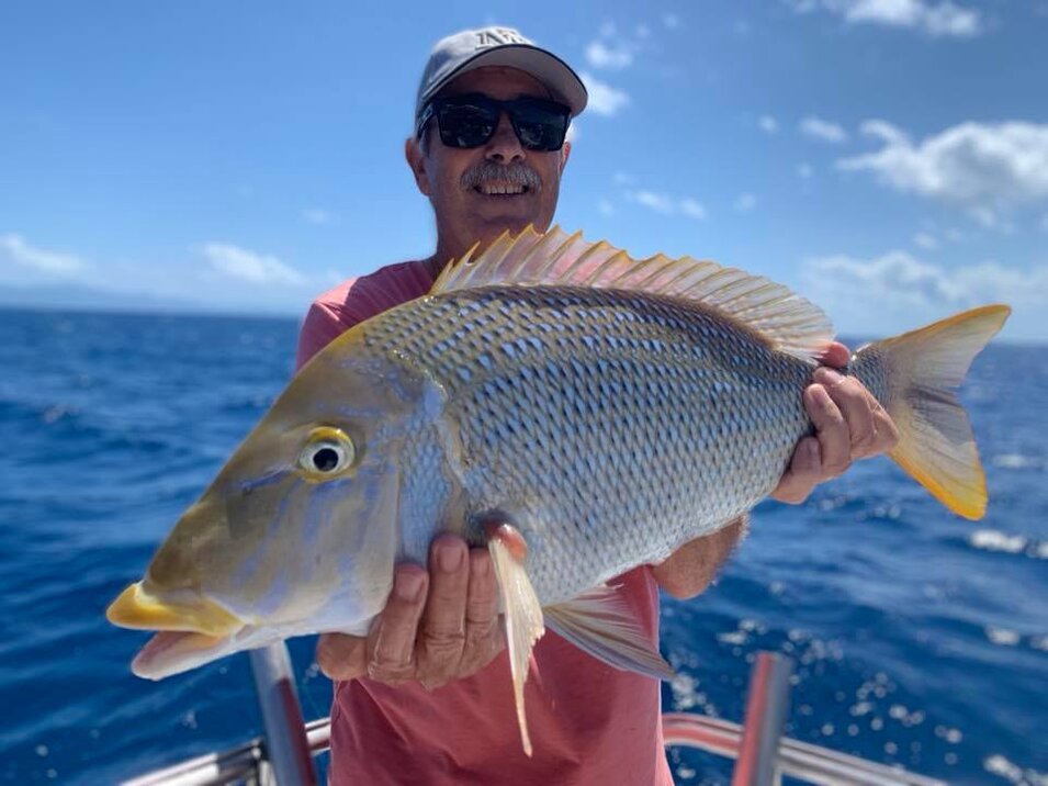 Male angler wearing white cap holding a reef fish