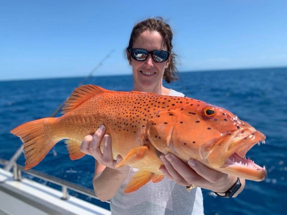 Female angler wearing black sunglasses holding a coral trout
