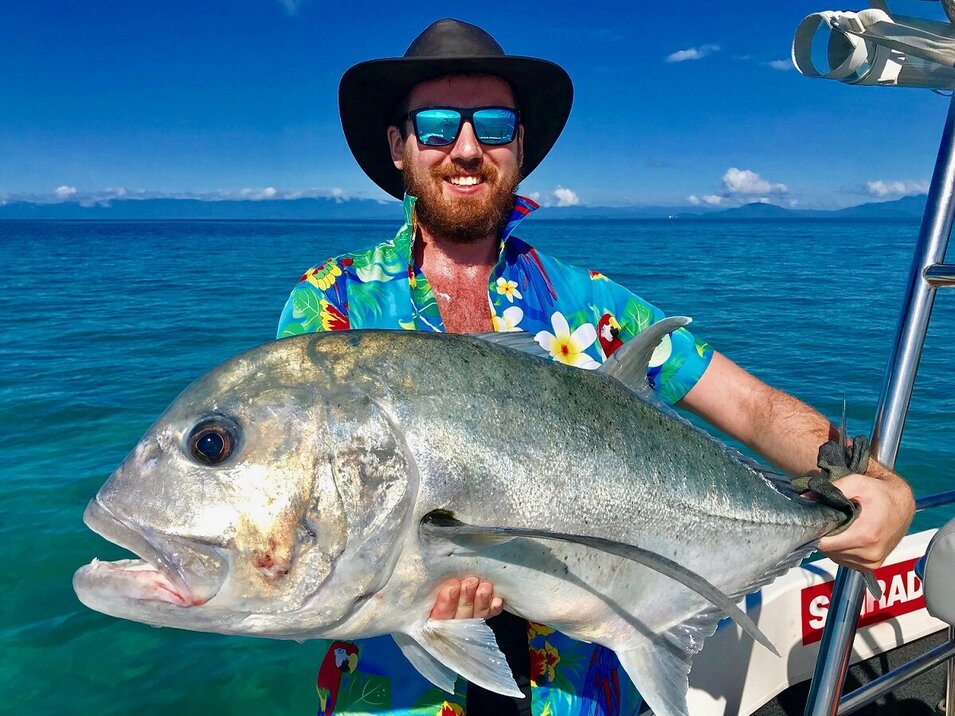 male angler wearing a Hawaiian shirt holding a trevally fish