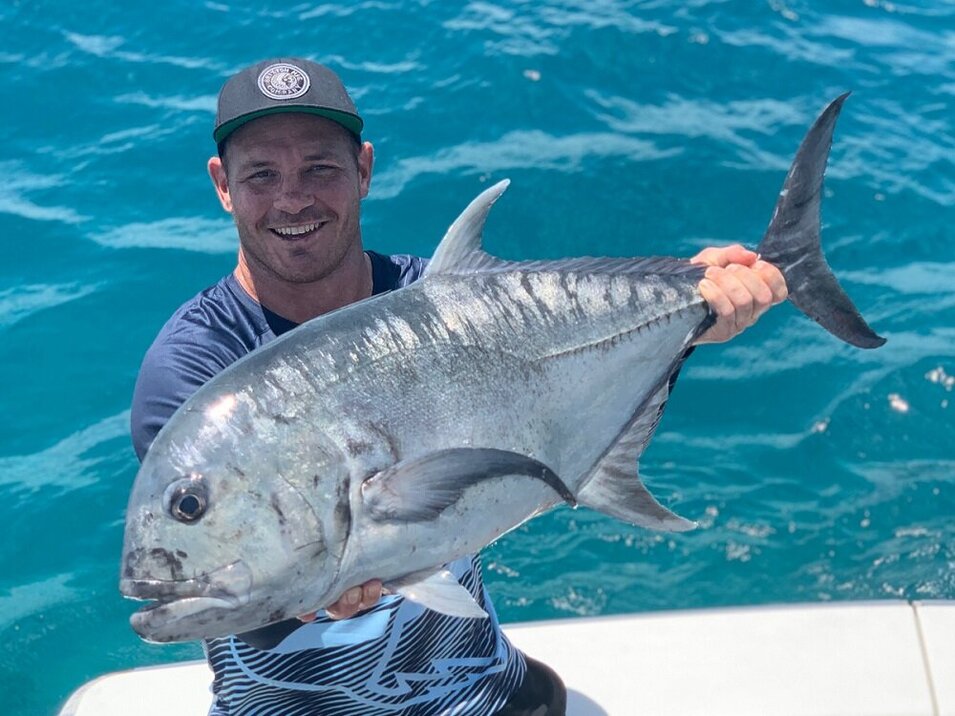 trevally fish held by a male angler wearing a cap