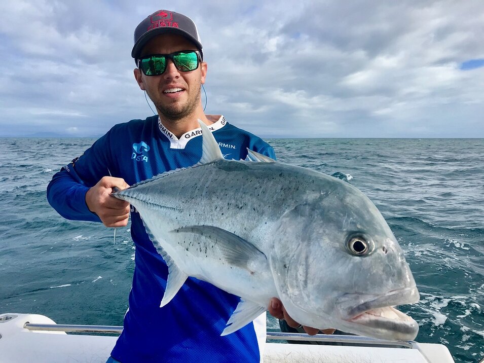 male angler wearing a blue shirt presents his trevally catch