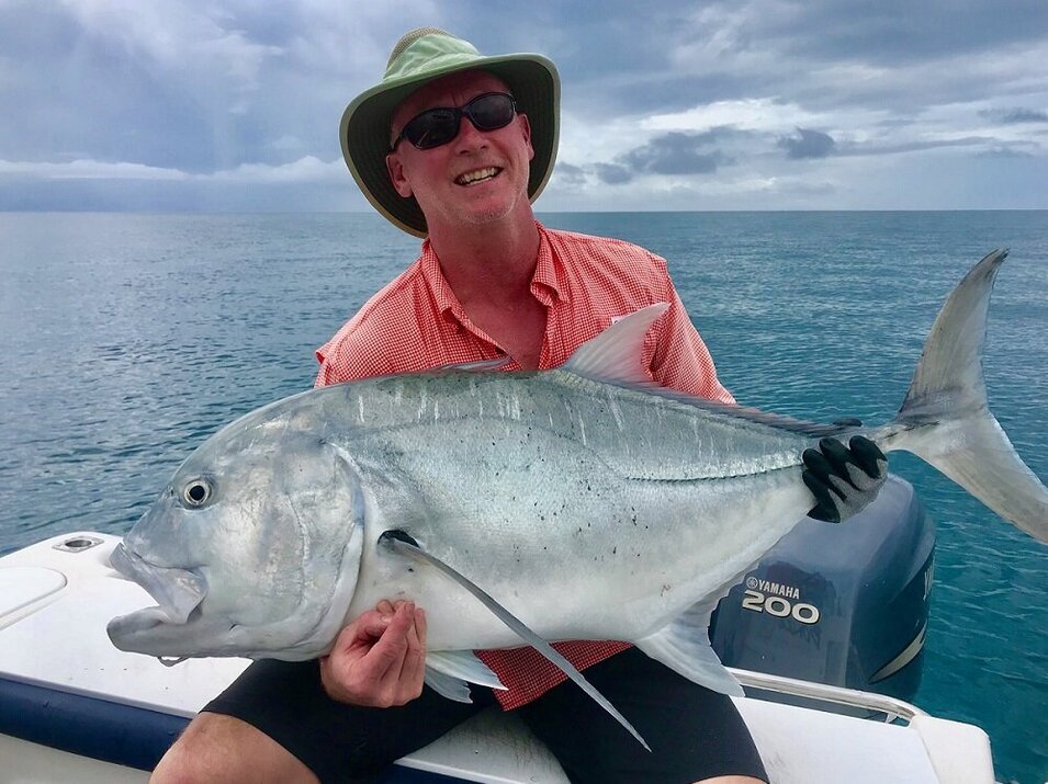 male angler wearing orange shirt with a trevally on his lap