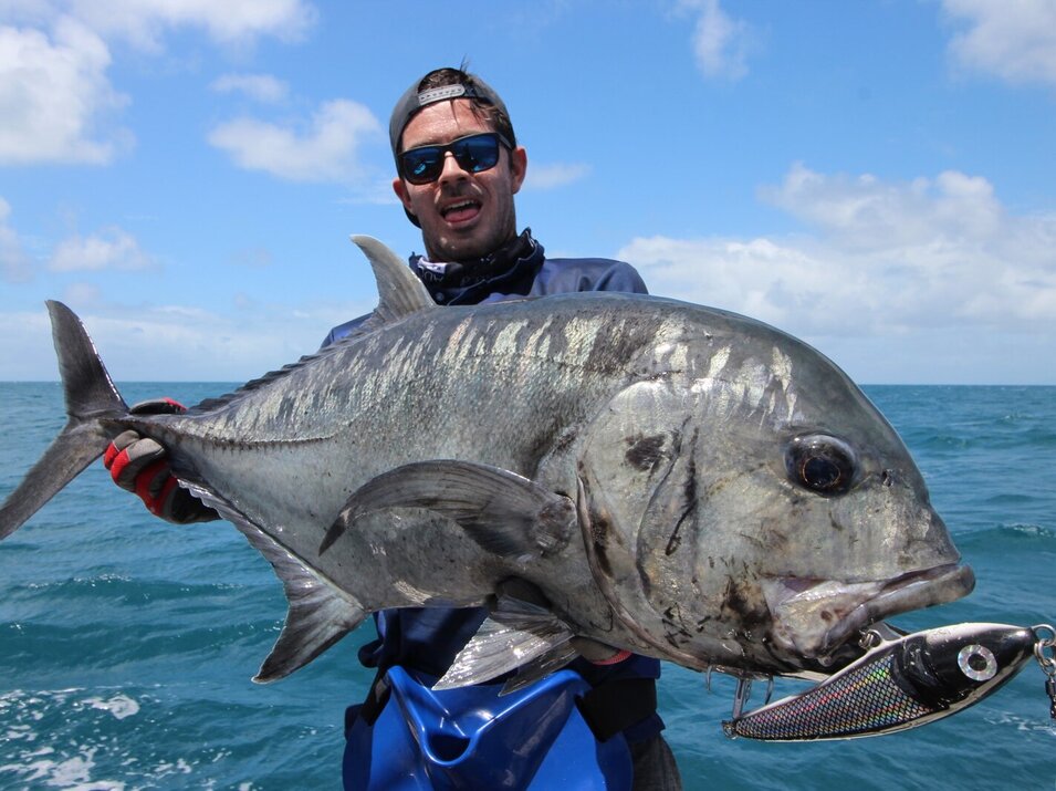 Male angler with cap holding a giant trevally