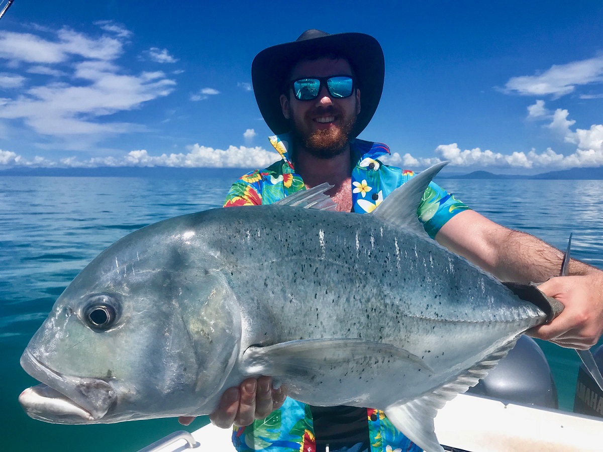 trevally fish held up by a male angler wearing a large sun hat