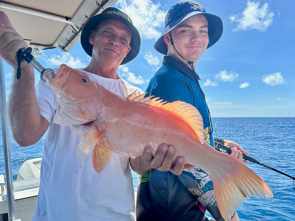 Two anglers on the Akula Sportfishing vessel, holding a Coral trout