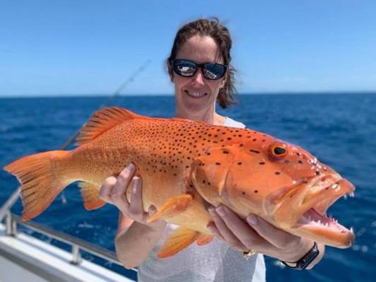 Girl with sunglasses holding a large orange coral trout