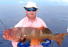 Reef angler wearing brim hat holding a large coral trout